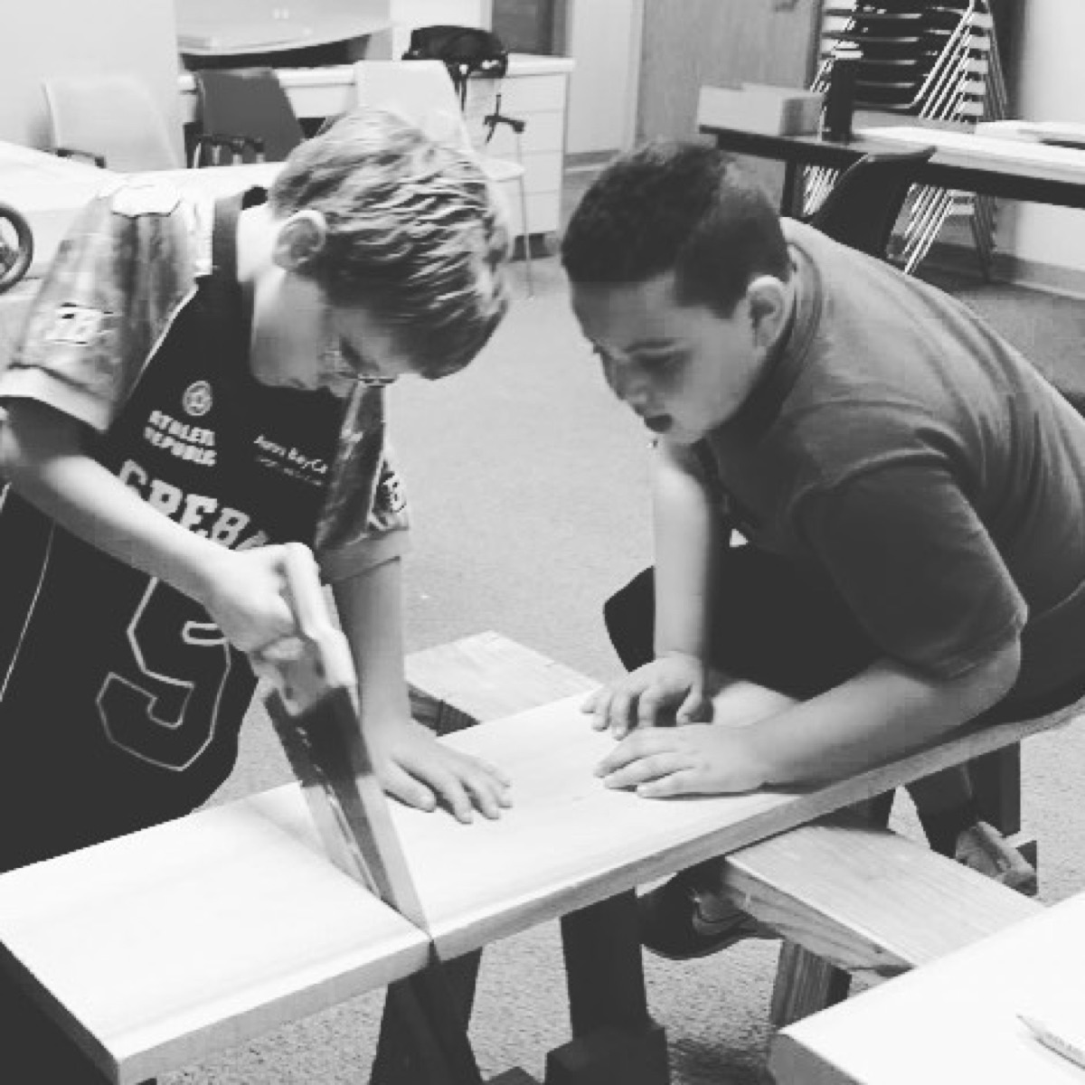 Students cutting wood together at a workbench