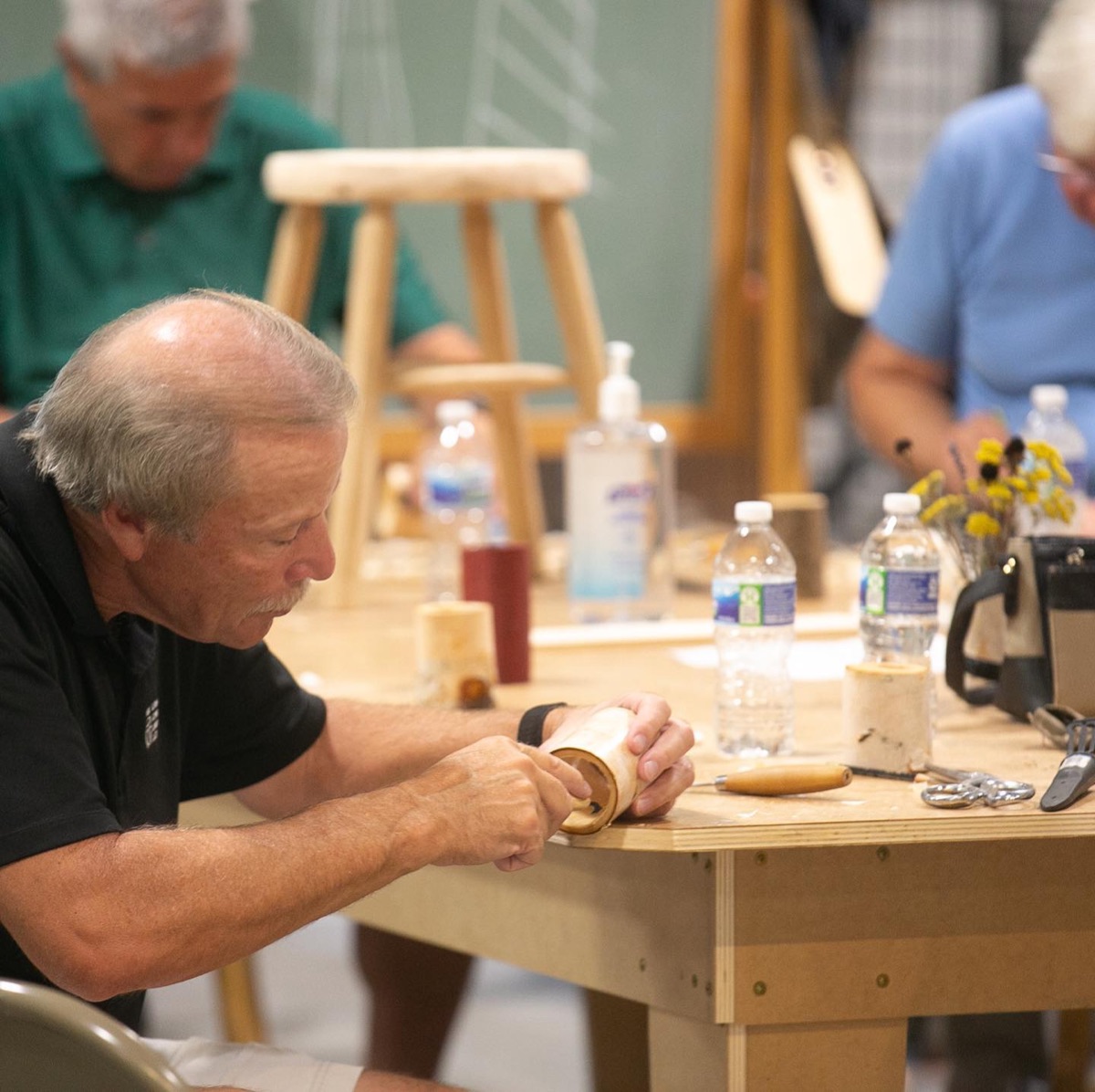 Adults working at a shared woodworking bench