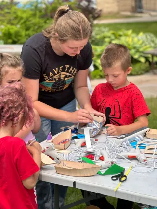 Volunteer helps children work on wooden model boats outdoors