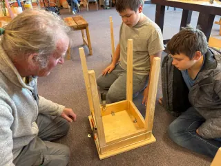 Adult instructor and two students inspect an upside-down wooden table