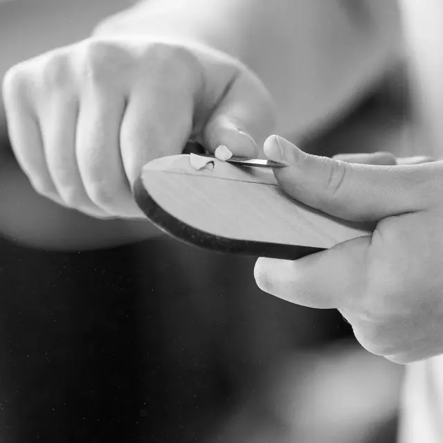 Hands shaping a wooden piece with a carving tool