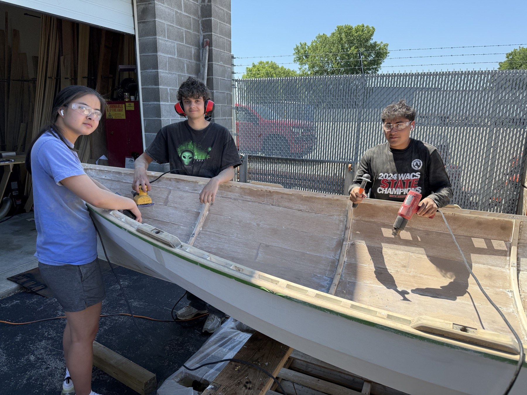 Three young people working on a wooden boat outside the Hands On Deck shop