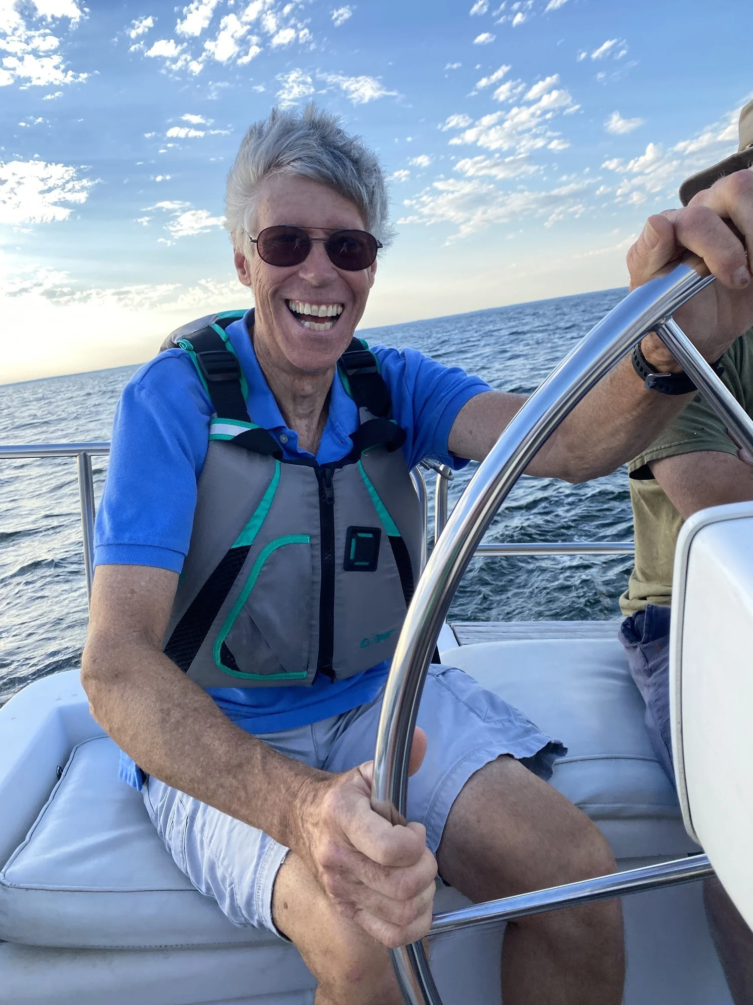 John Seaman smiles while steering a sailboat on open water.